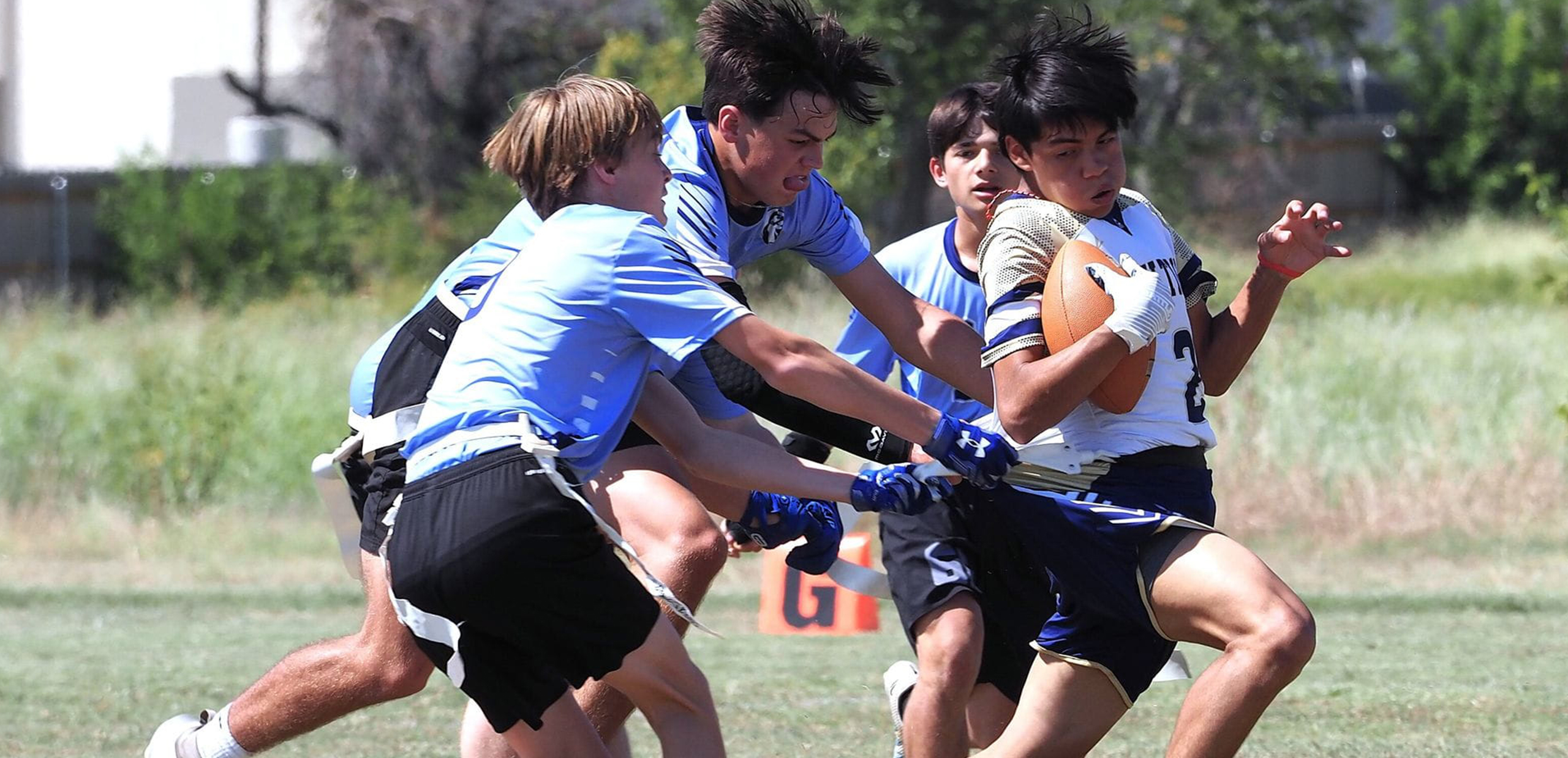 high school student running with the ball during a flag football game while defenders reach for his flag.