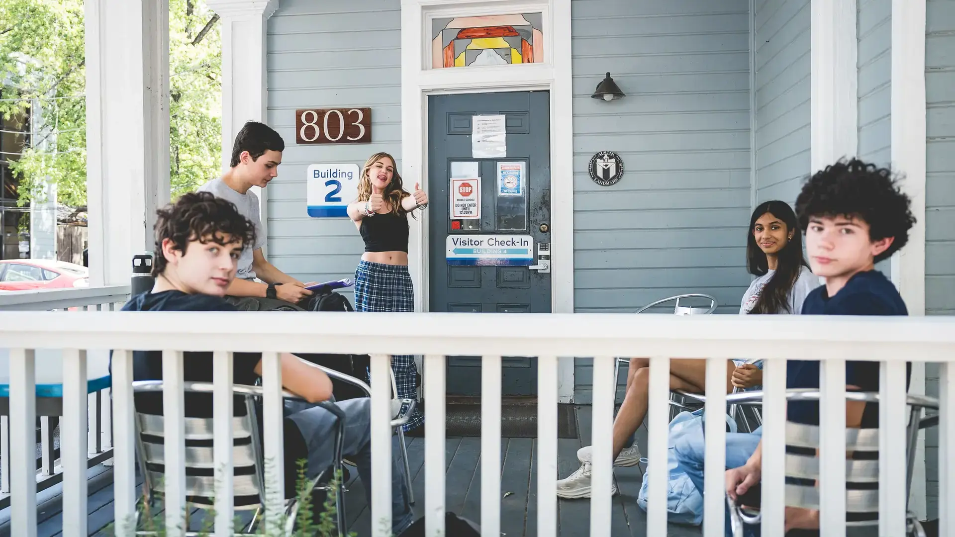 High school students relaxing and talking on the porch outside a campus building.