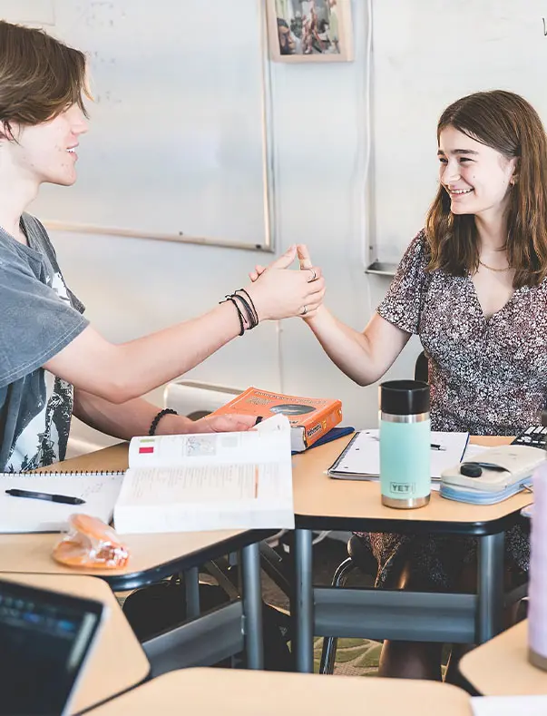 Two high school students are sitting in math class having a thumb war.