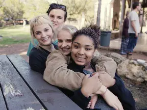 Four Headwaters School students sit together at a picnic table outdoors, smiling and leaning close during the Forward.