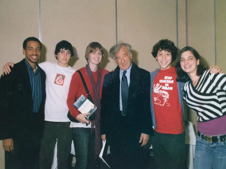 Group photo of students standing with an older man in a suit, indoors.