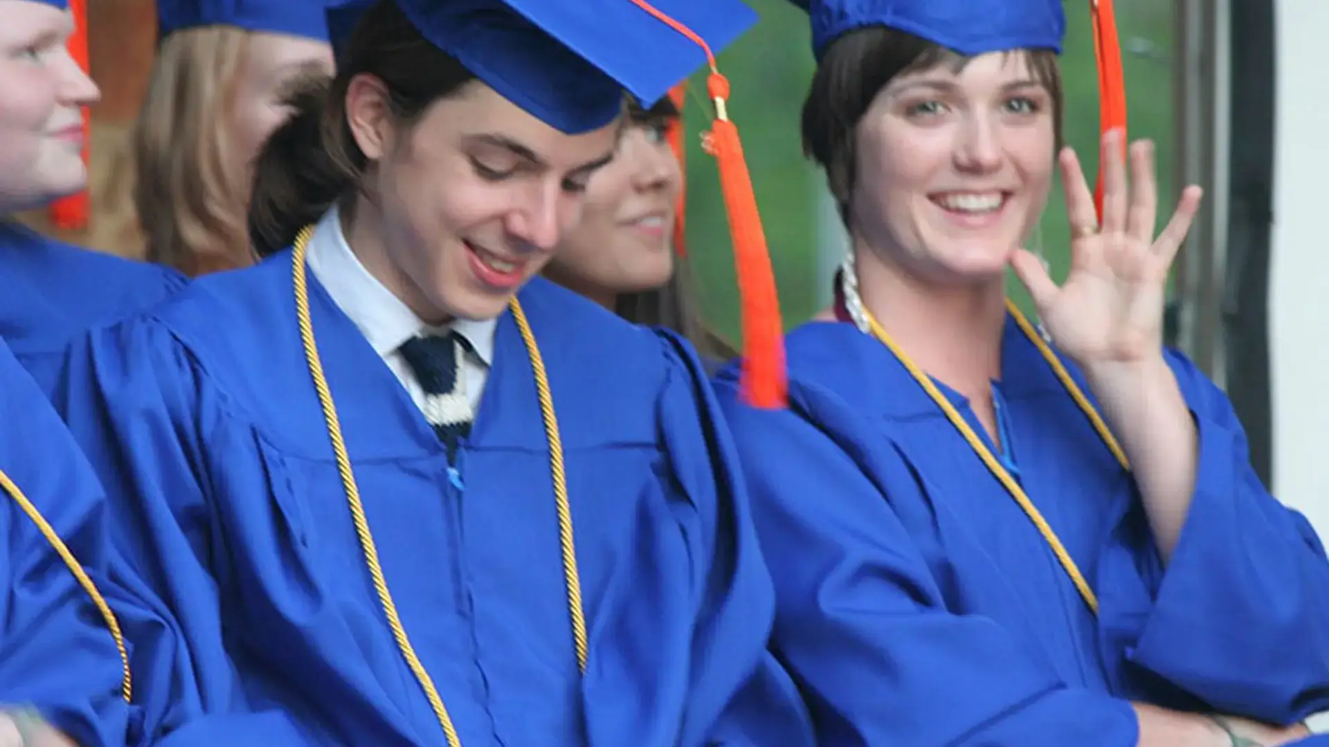 Graduates in royal blue caps and gowns smiling and waving.