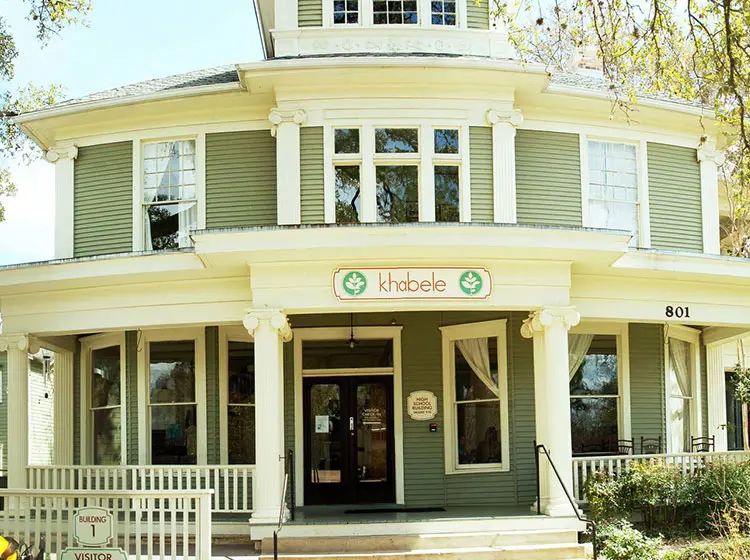 Exterior of the historic Khabele school building with a green Victorian facade and covered front porch.