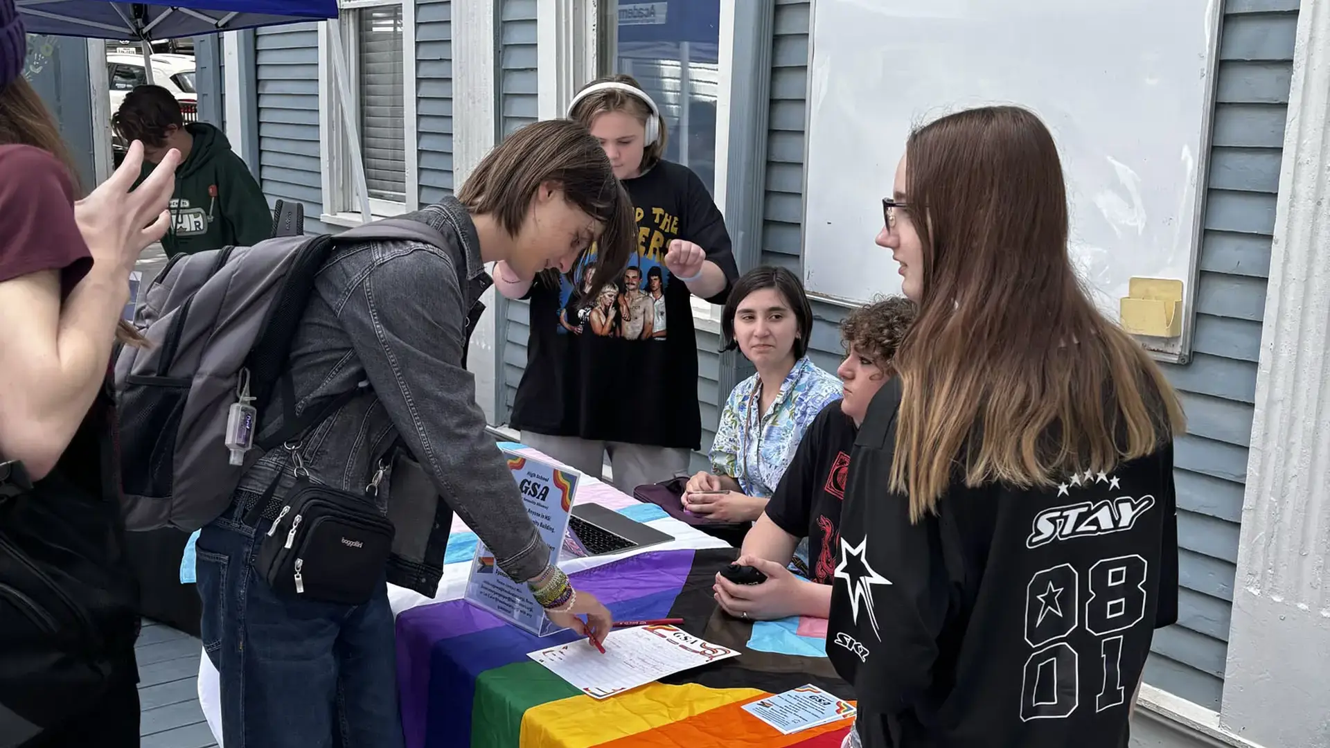 Middle and High School students interacting at a student club information table during a campus event.