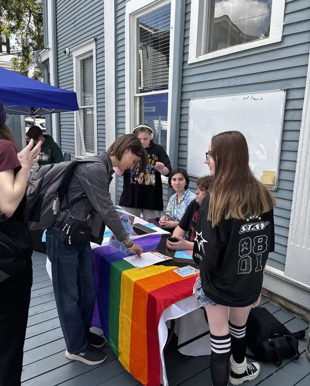 Middle and High School students interacting at a student club information table during a campus event.