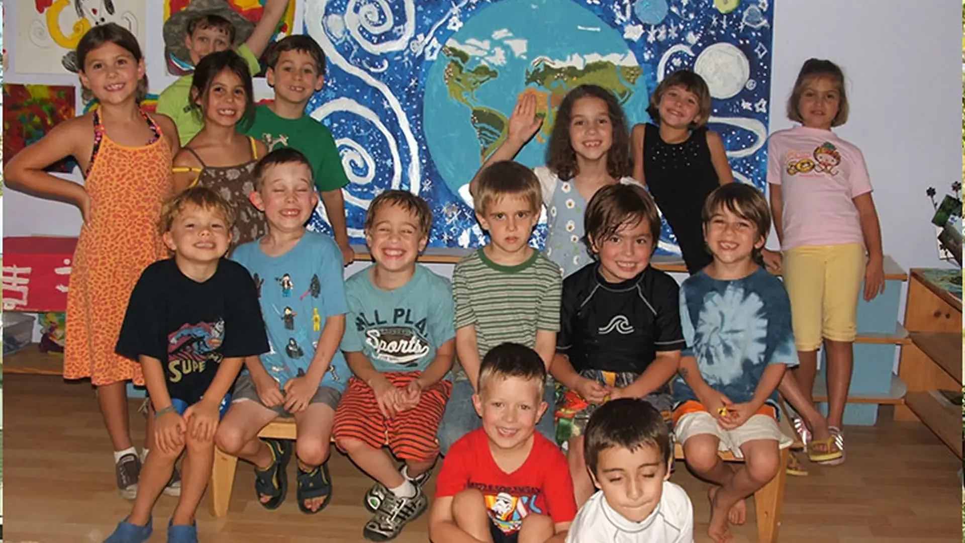 Group of children posing together indoors in front of a colorful mural.