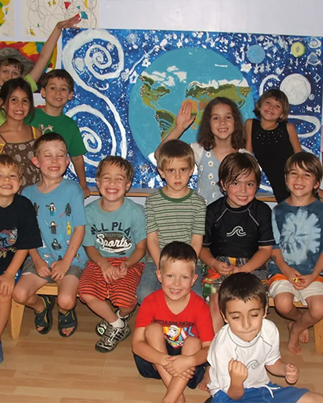 Group of elementary school children posing together in front of a painted Earth mural