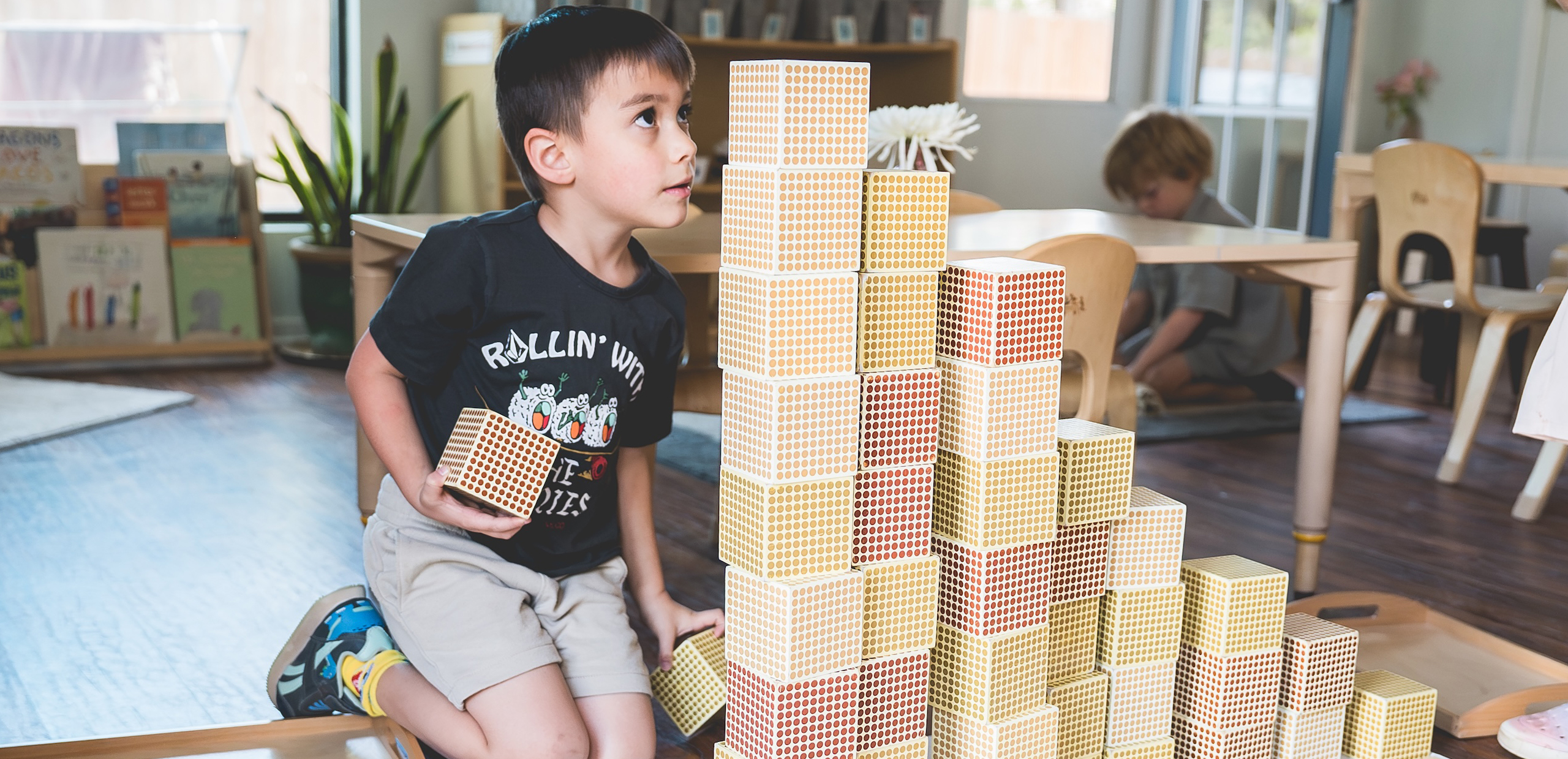 oung child stacking Montessori hundred-square cubes to build a tower in the classroom.