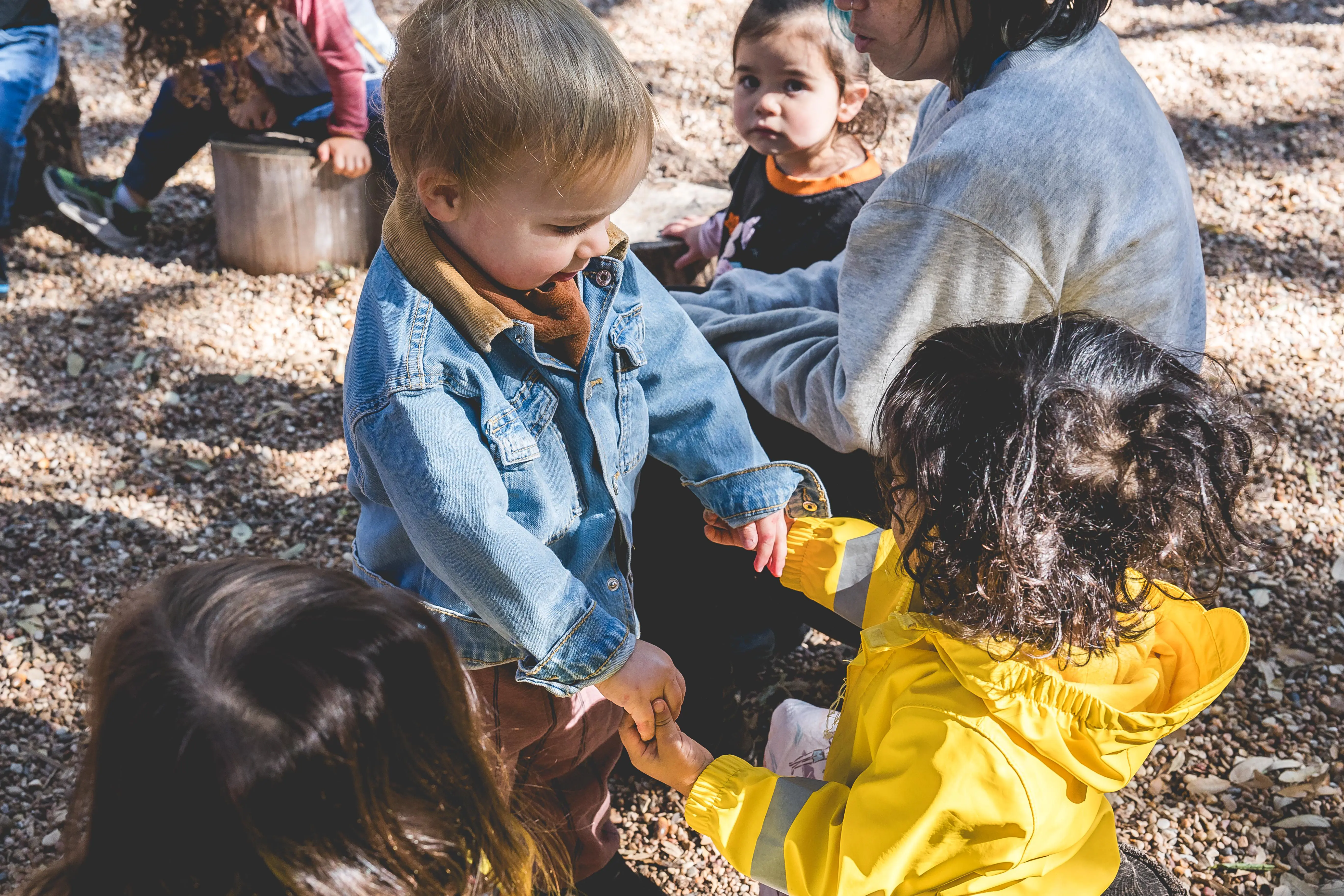 Young Children’s Community students interact and hold hands during outdoor play while gathered with classmates and a guide.