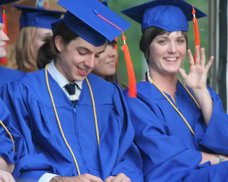 high school graduates in caps and gowns smiling and waving during commencement.