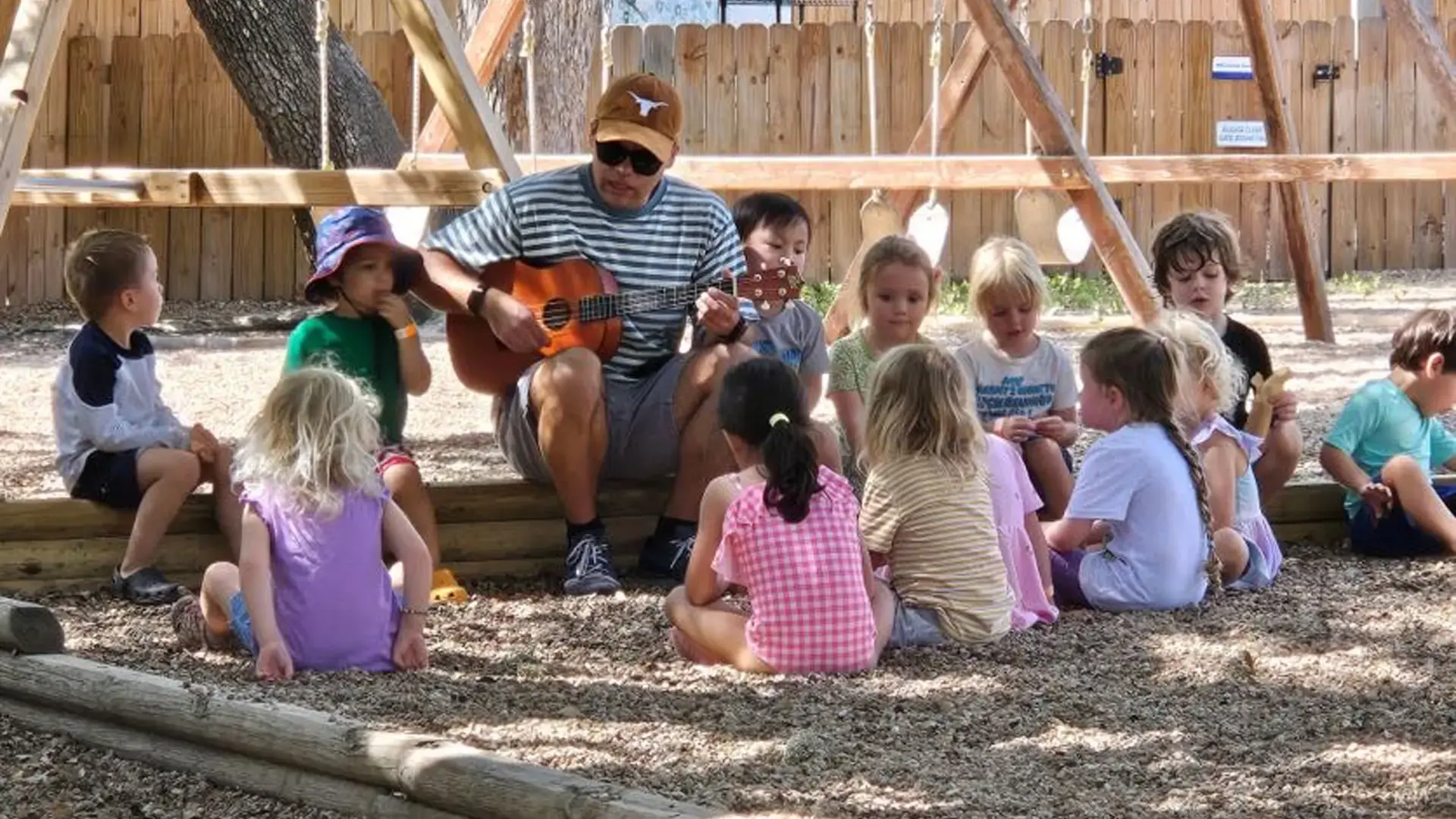 A teacher reading to young children seated together outdoors during summer camp.
