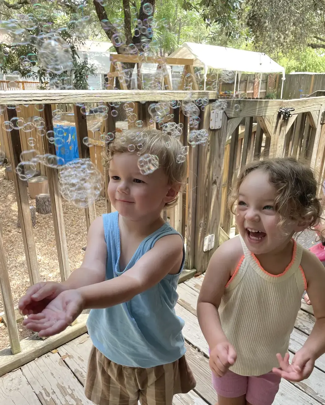 Two young children laughing and playing with bubbles on an outdoor deck