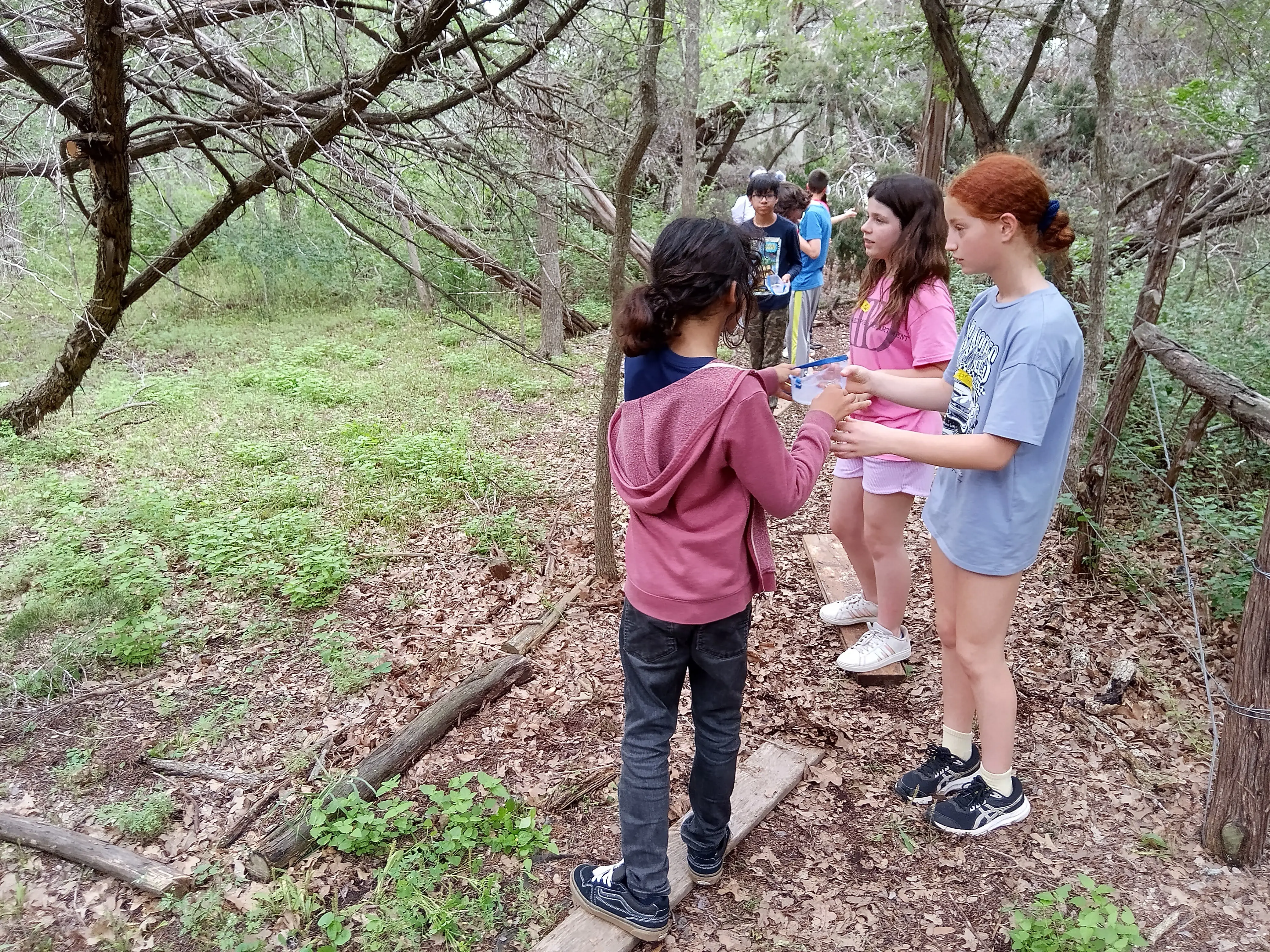 Students standing together in a wooded area surrounded by native Texas trees.