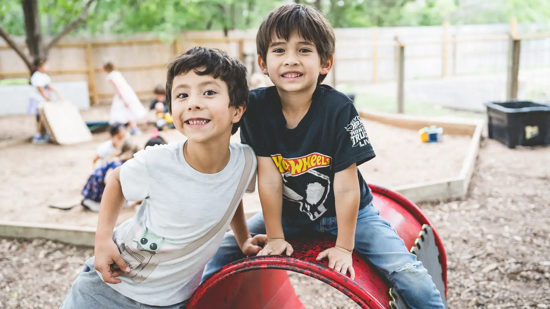 Two young students smiling while playing together on outdoor playground equipment.