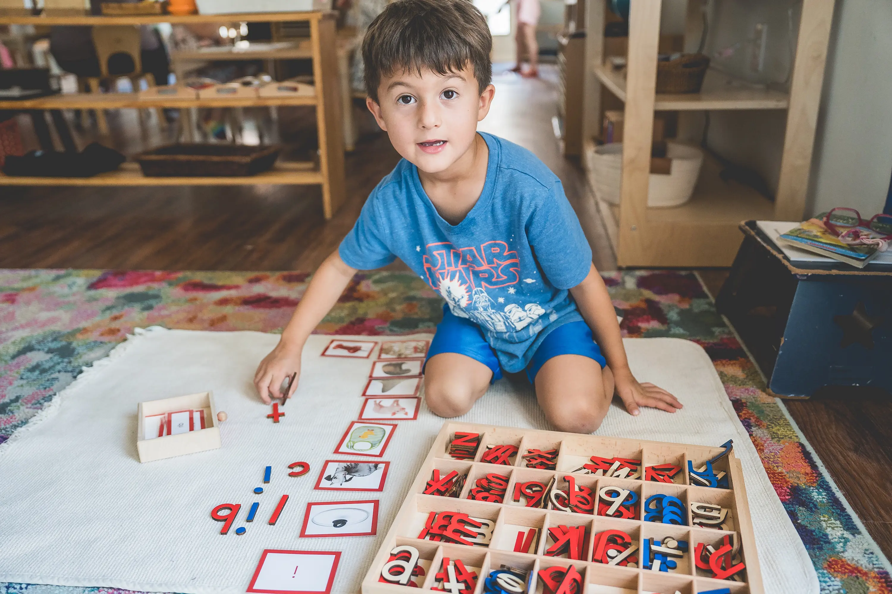 A young student works with Montessori language materials and a moveable alphabet on a classroom mat in an Early Childhood classroom at Headwaters School.