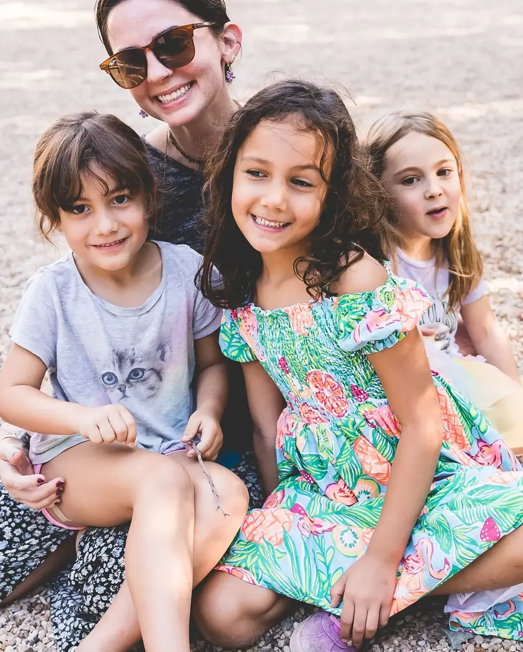 A teacher smiling with three young students seated together outdoors on a playground.