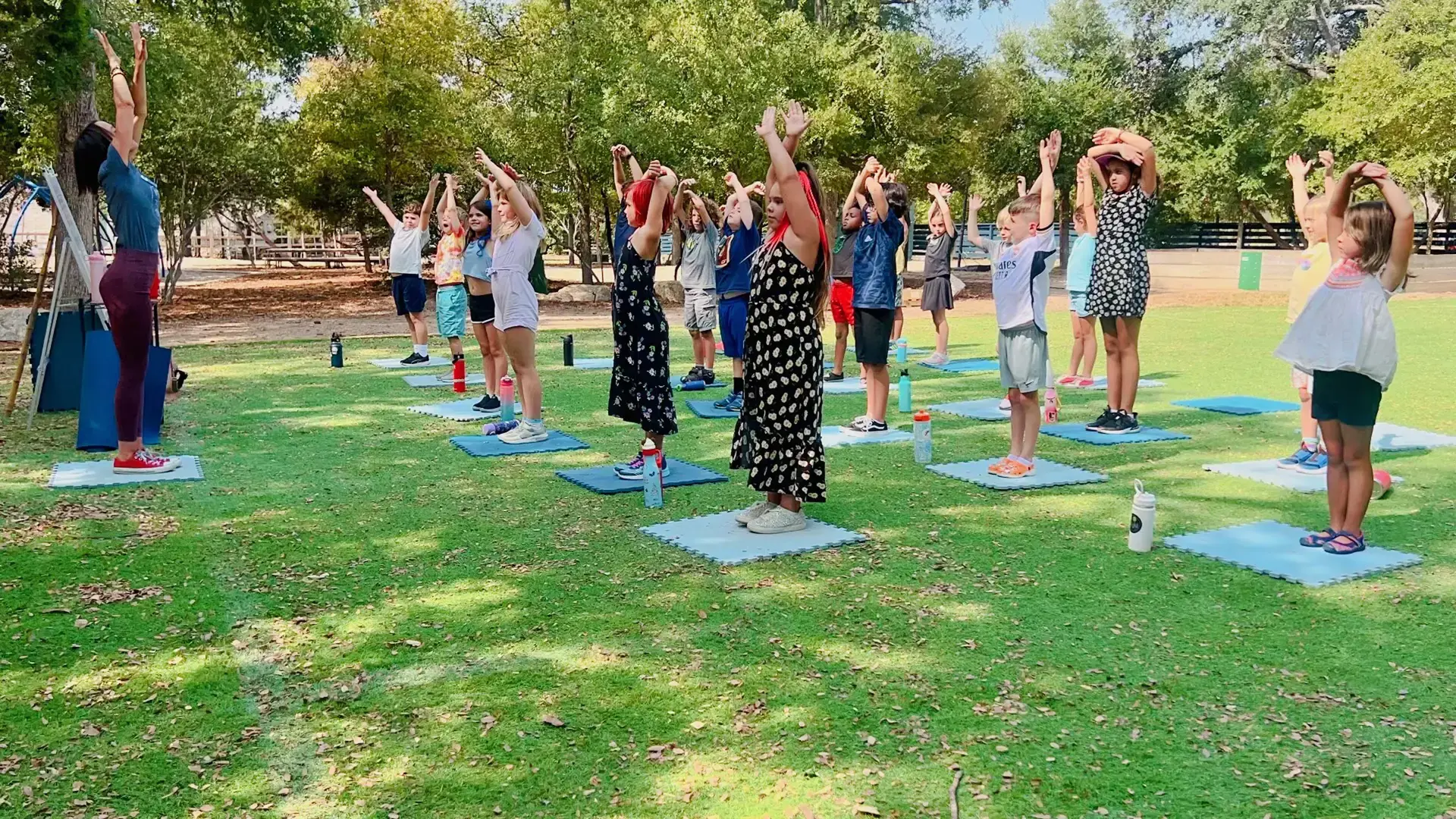 elementary students stretching together outdoors on mats during a health and fitness class.