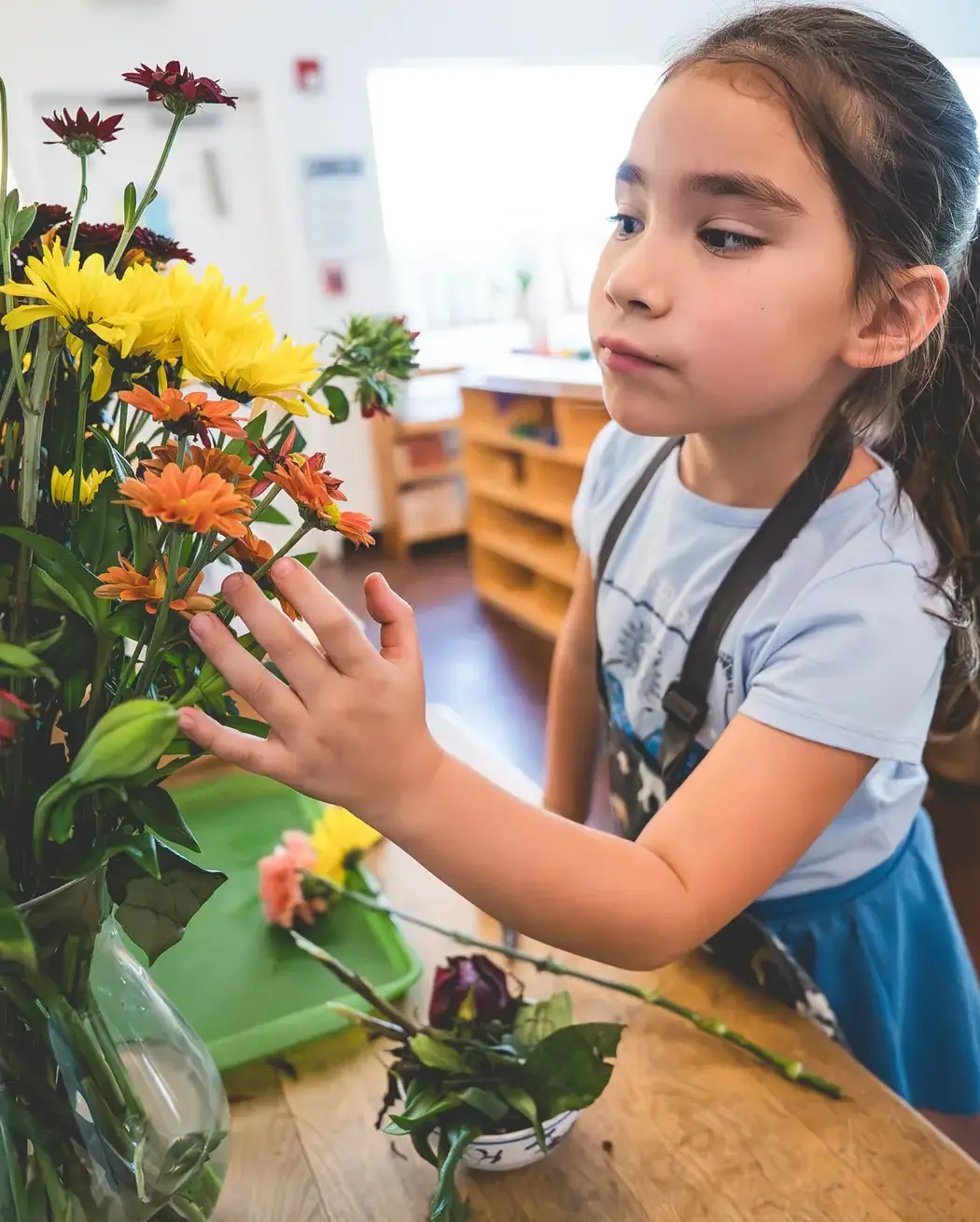a young child arranging colorful flowers in a classroom.