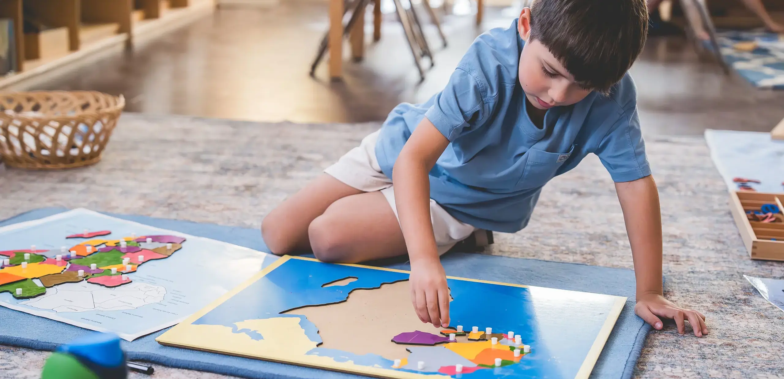 Elementary student working with a Montessori geography puzzle map on the classroom floor.