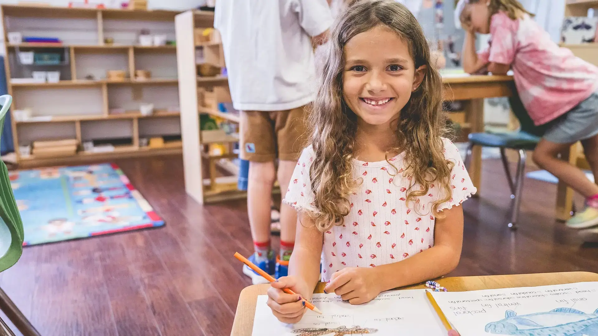 an elementary student smiling while working on schoolwork at a desk.
