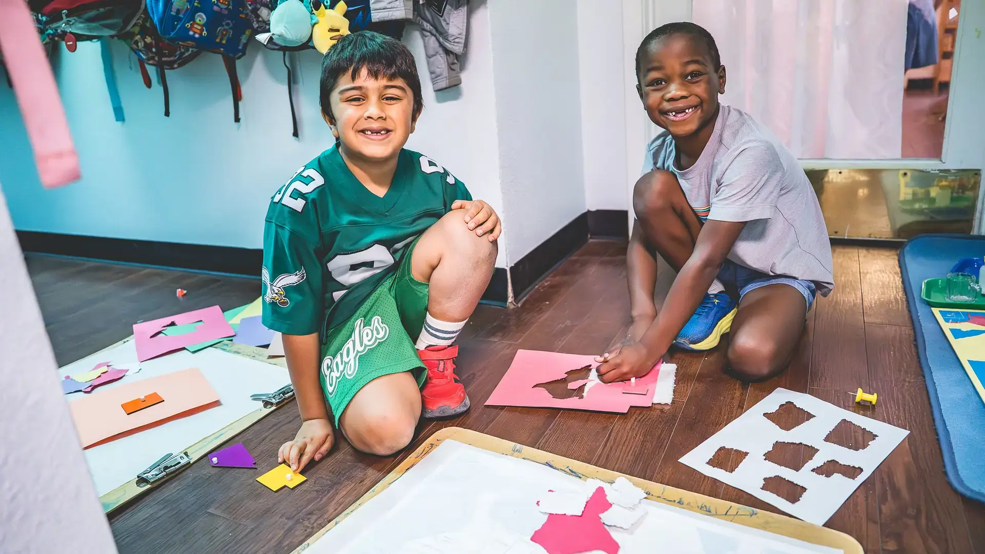Elementary students working on a cutting and shapes art project at a table.