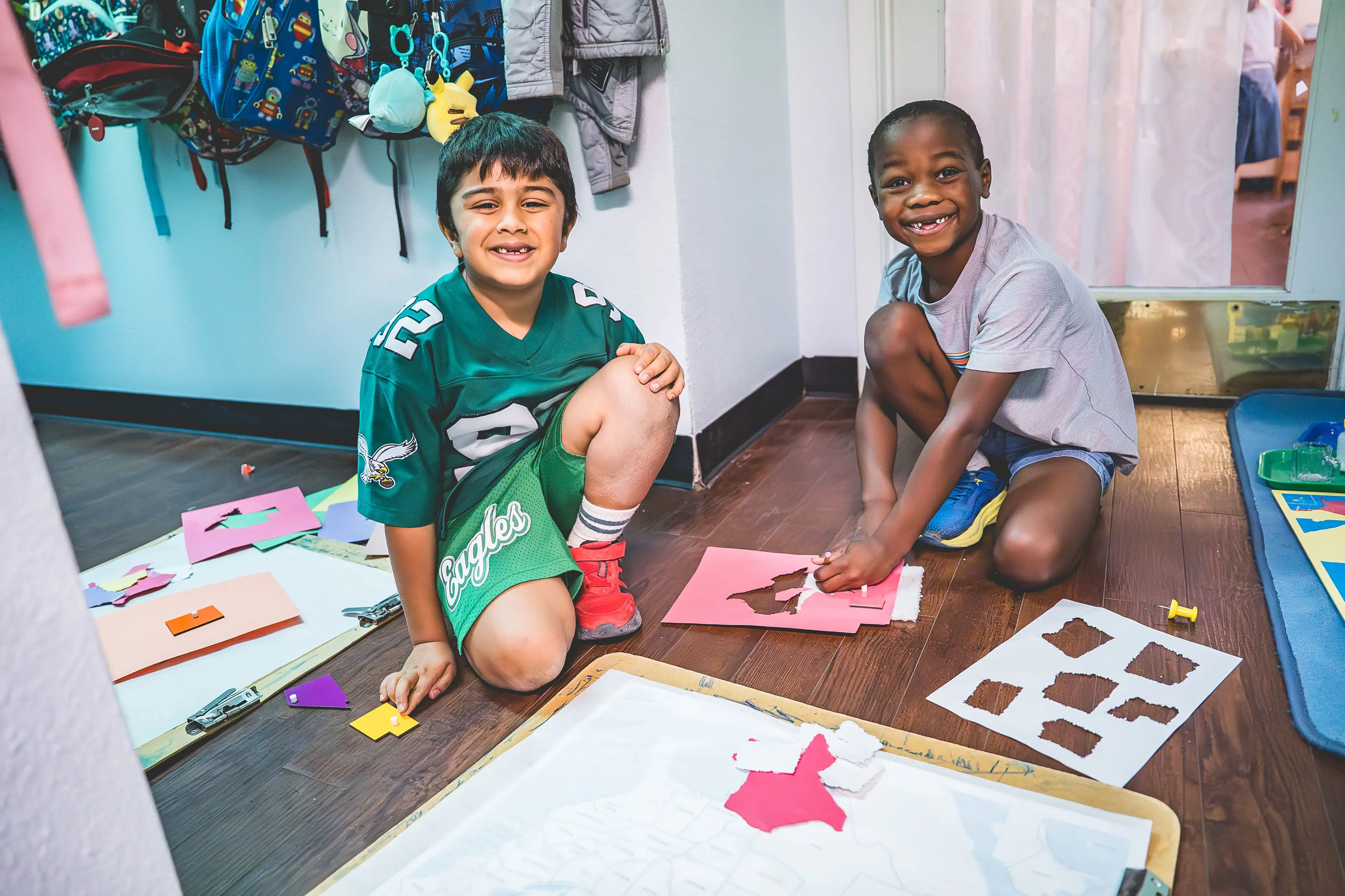 Elementary students cutting shapes and working with hands-on materials on the classroom floor.