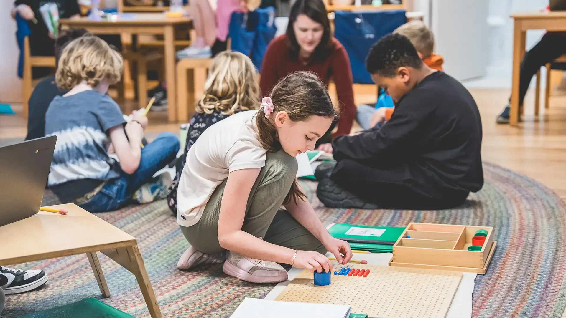 elementary students working on the floor with a Montessori bead board for a math activity.
