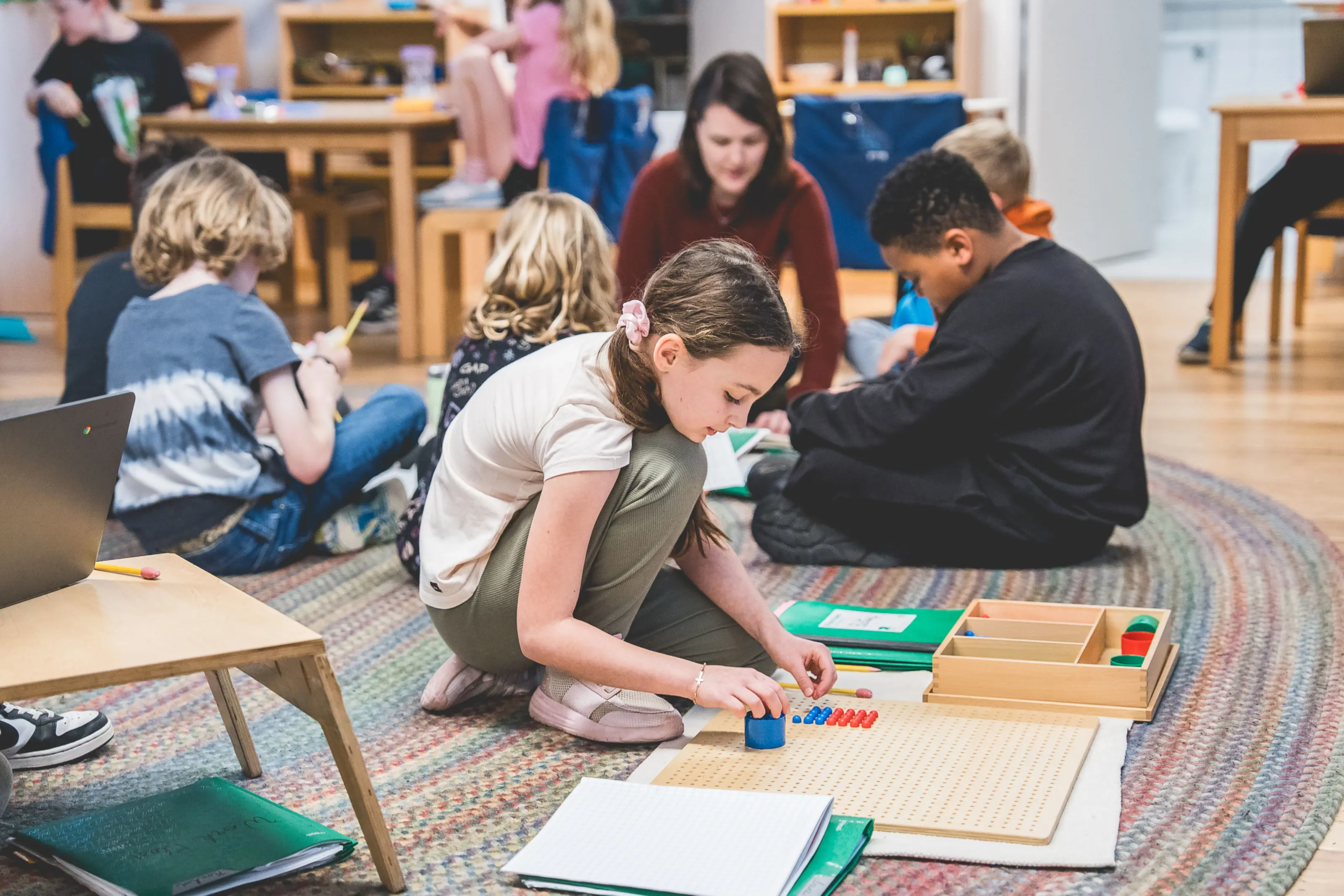 elementary students working with math bead materials on the floor.
