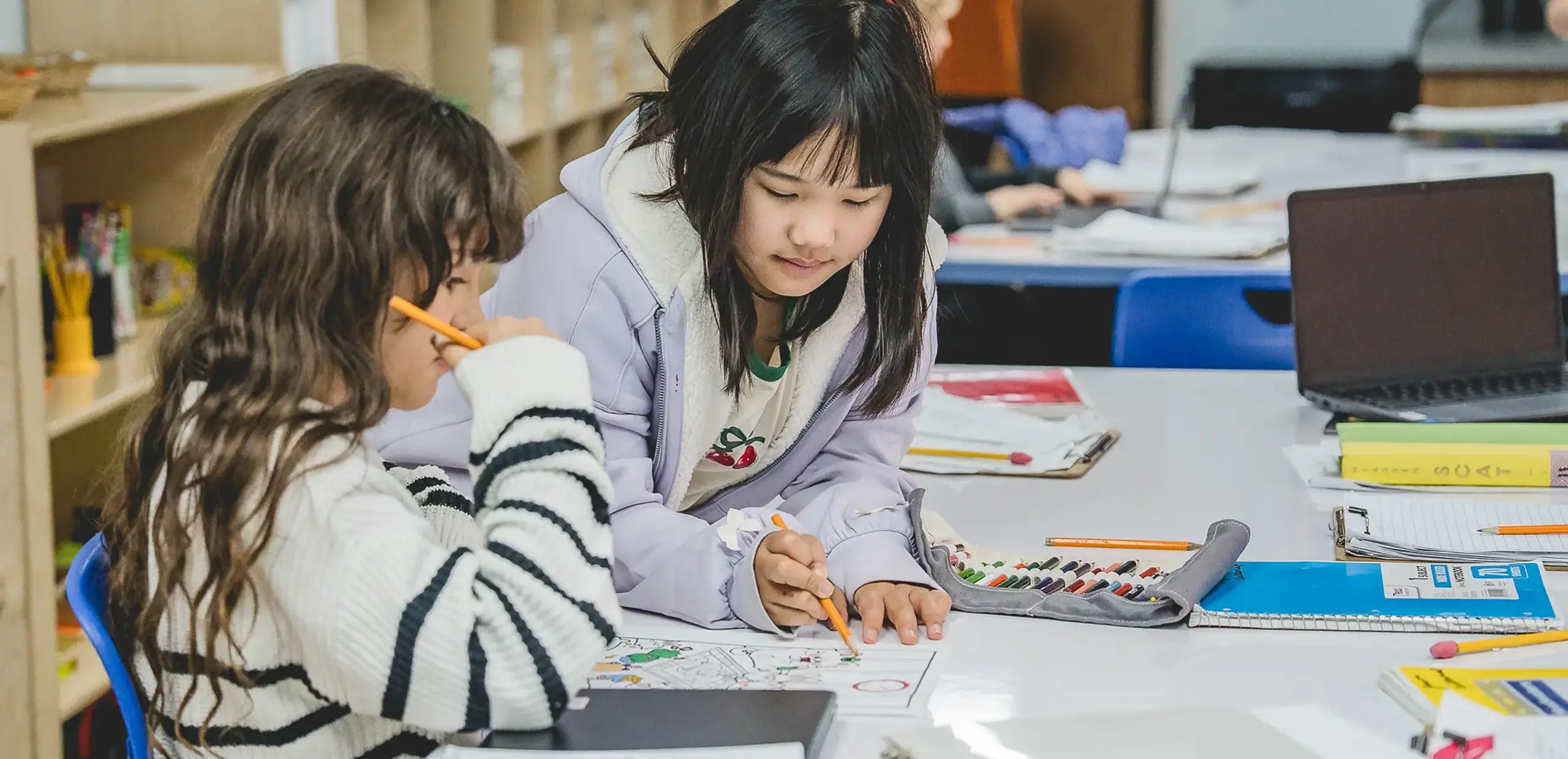 elementary students working together on a coloring assignment at their classroom desk.
