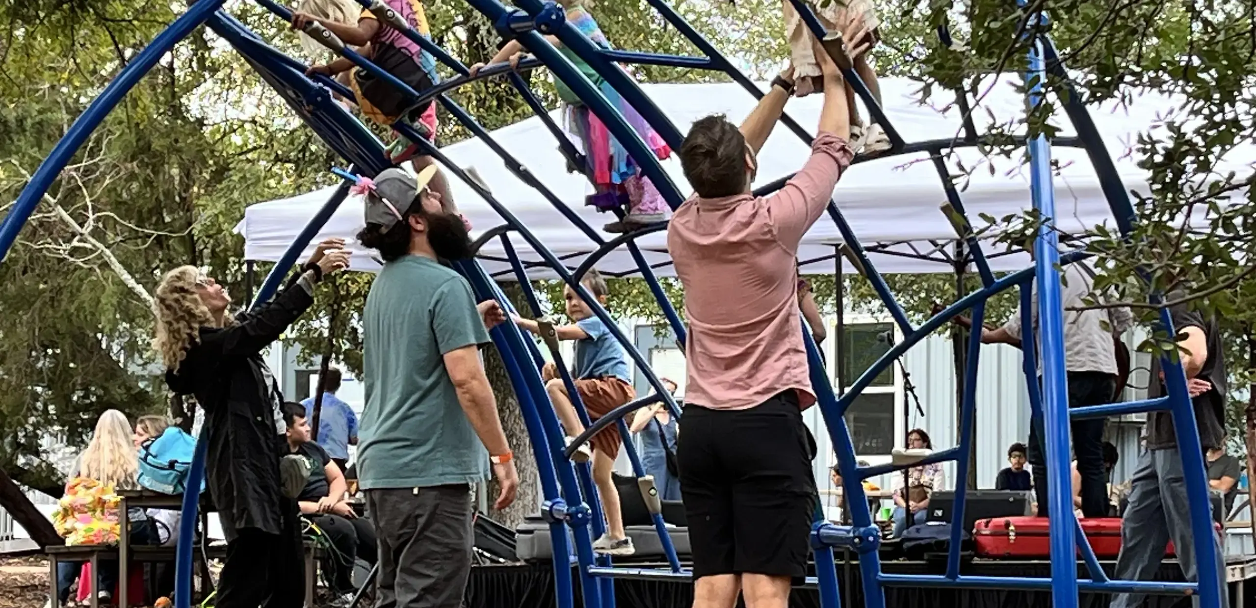 children climbing a dome play structure with parents assisting during the Headwaters Fall Fest.