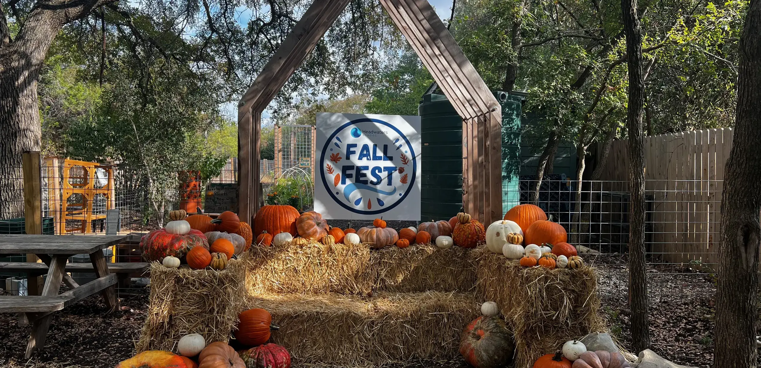 pumpkins displayed on hay bales beneath a wooden archway with a Headwaters Fall Fest sign.