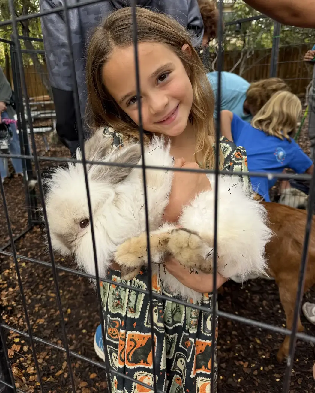 student smiling while holding a fluffy white rabbit at a petting pen during the Headwaters Fall Fest.