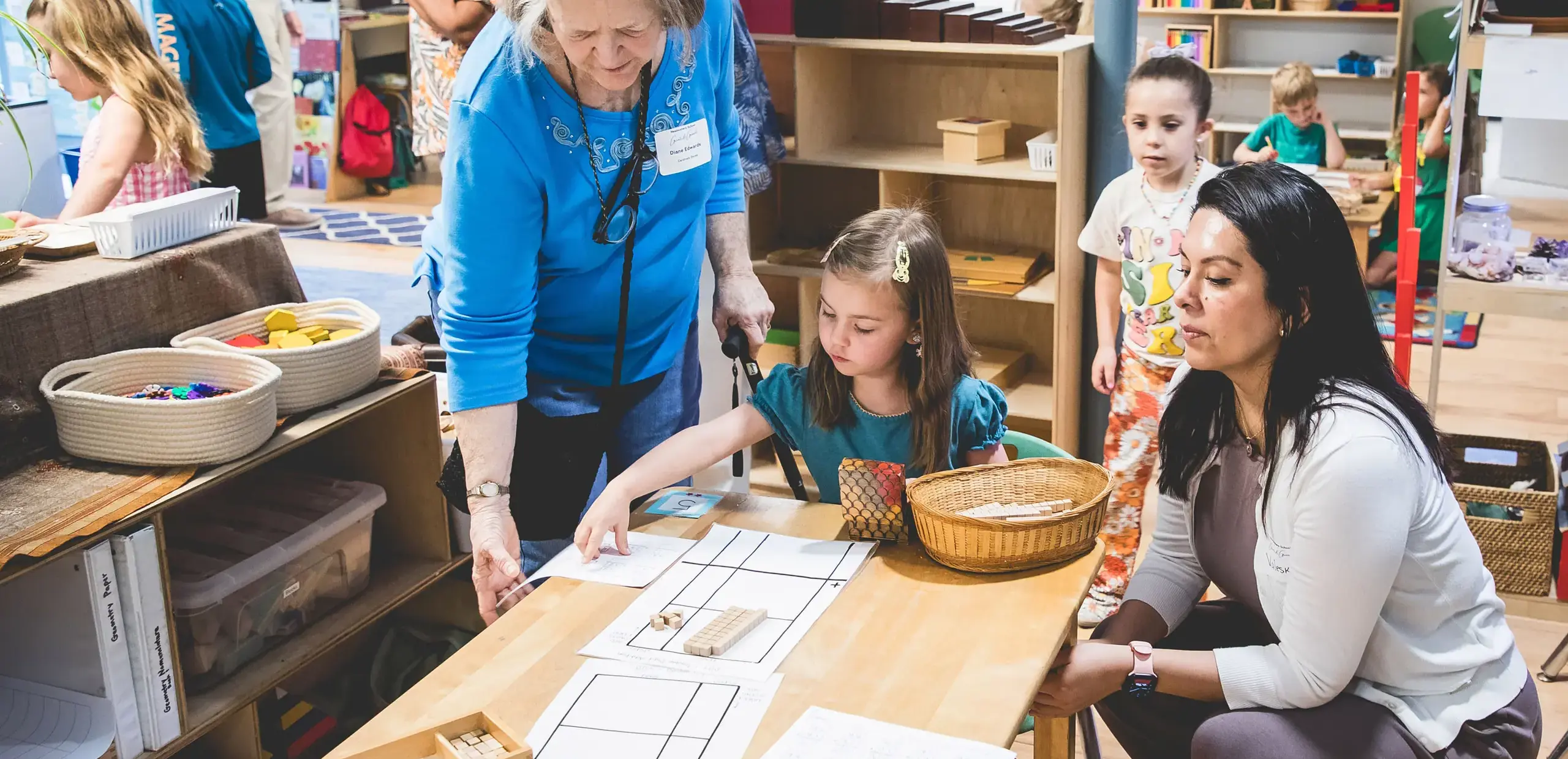 elementary student demonstrating a Montessori math lesson to a grandparent during Grandparents and Special Friends Day.