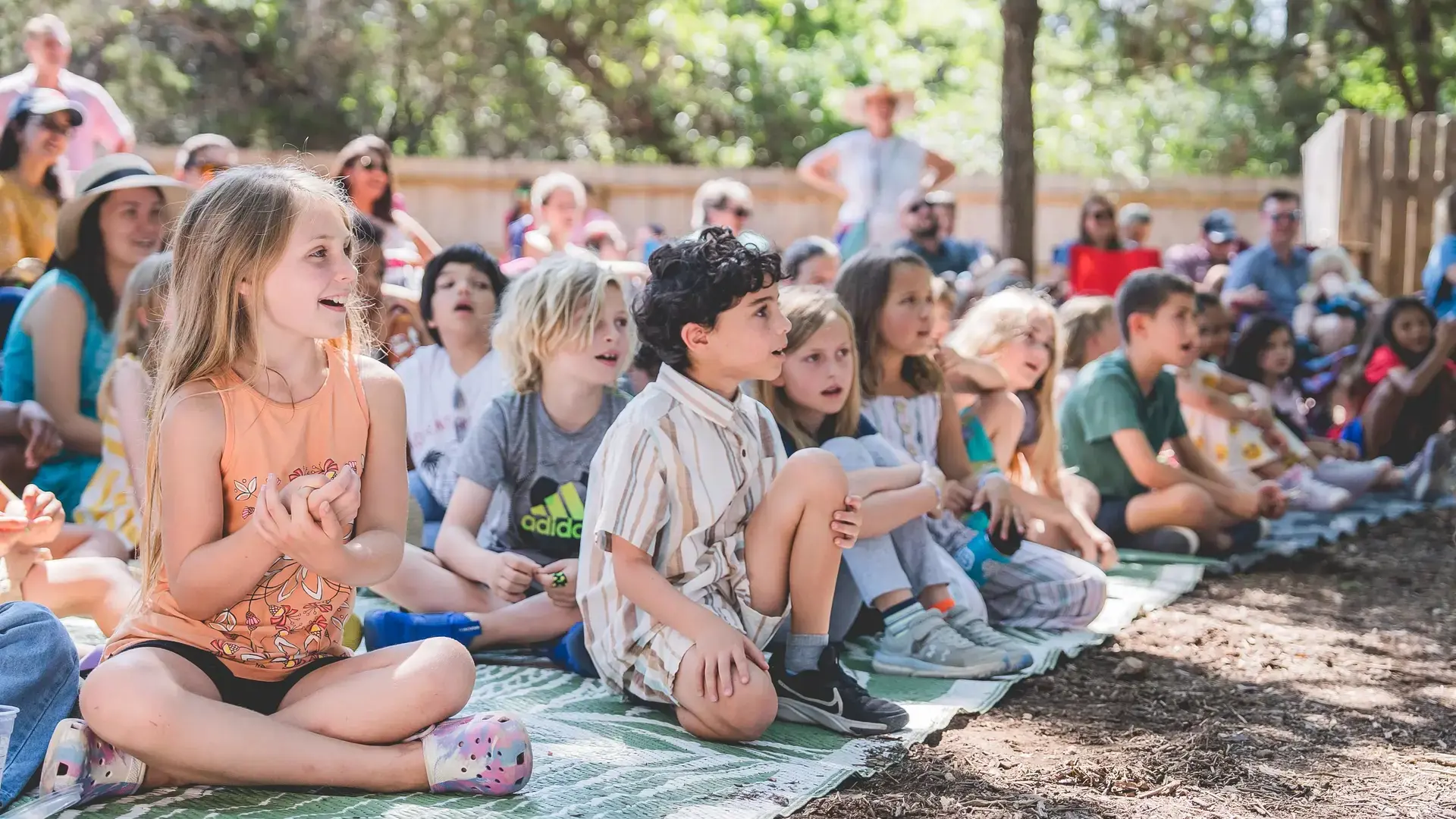 Elementary students sitting together outdoors during a group lesson.