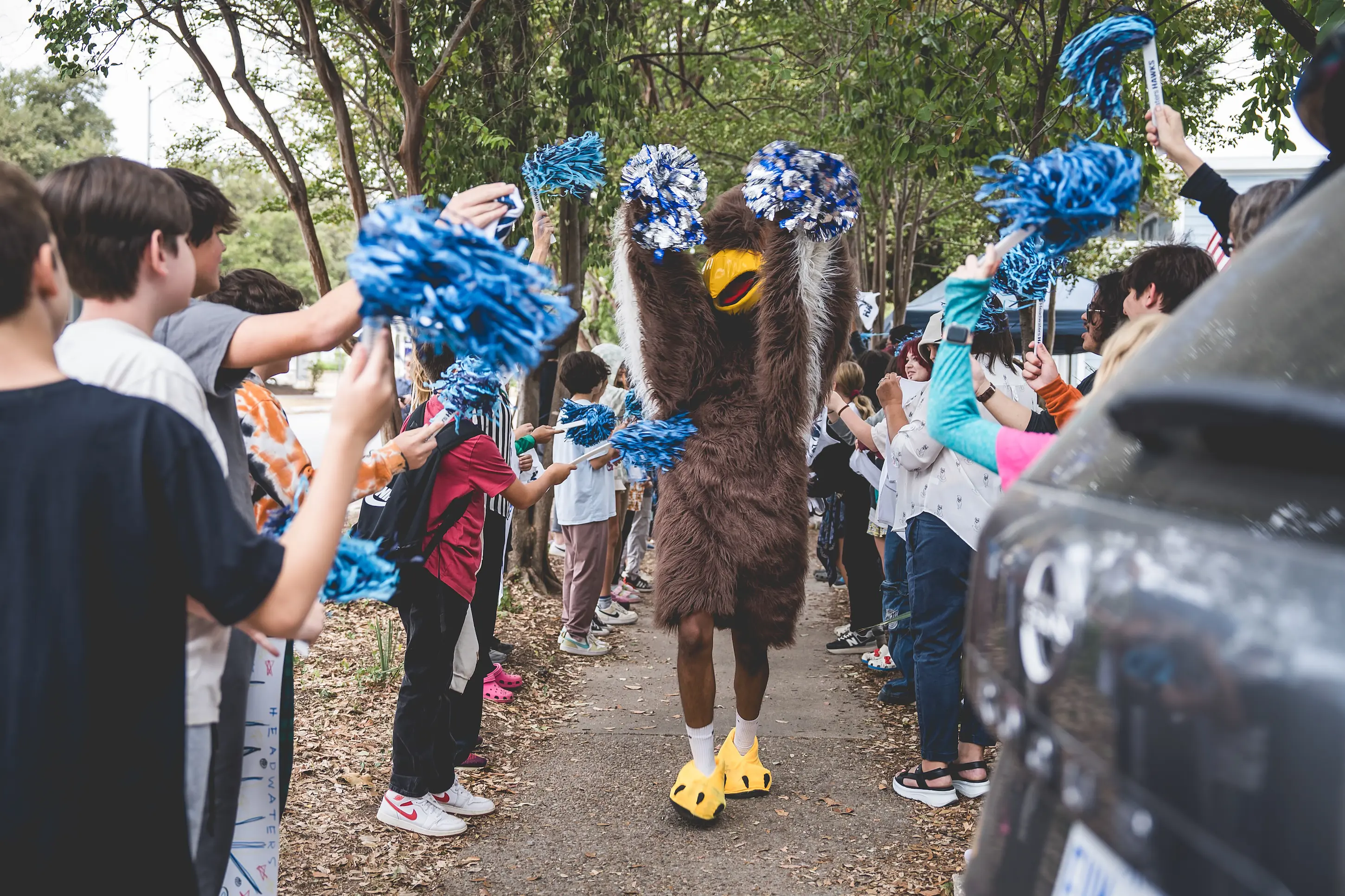 Headwaters School students cheer with blue pom-poms as the Hawk mascot walks through a tunnel of school spirit at the River Campus.