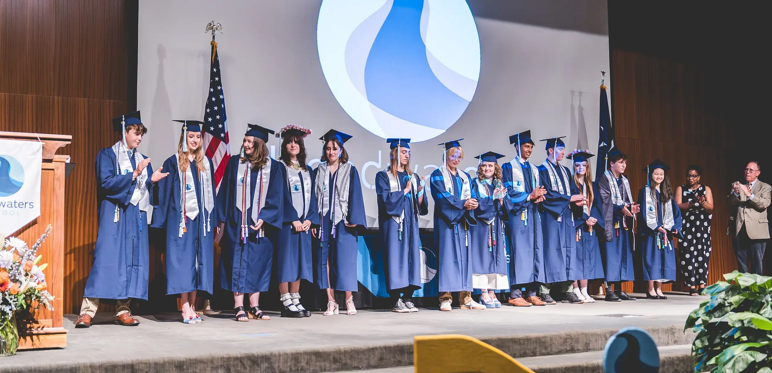 Headwaters School graduates in navy caps and gowns standing on stage during the commencement ceremony.