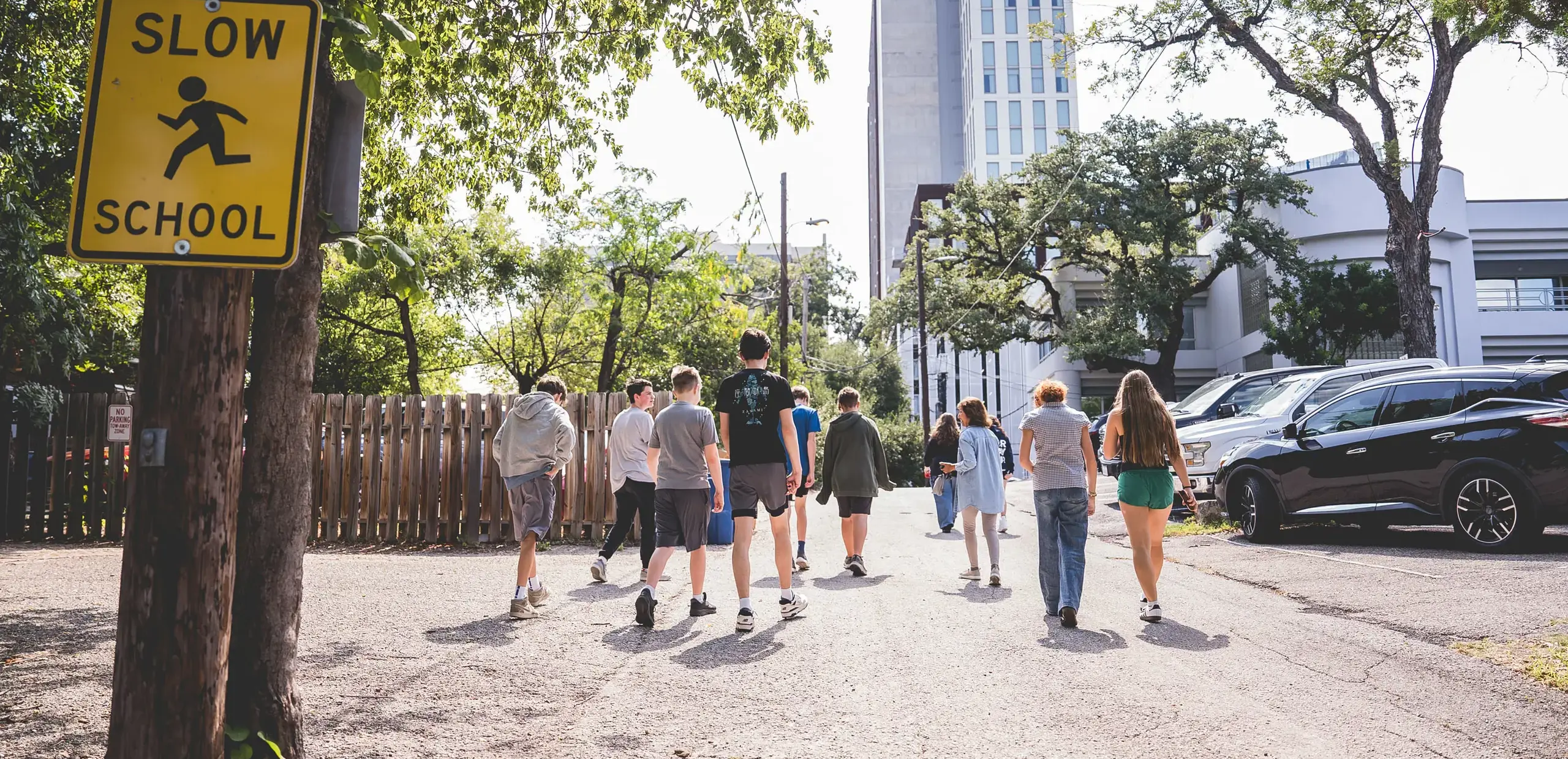 High school students walking down a downtown Austin street past a school crossing sign, part of Headwaters School's city-as-classroom program.