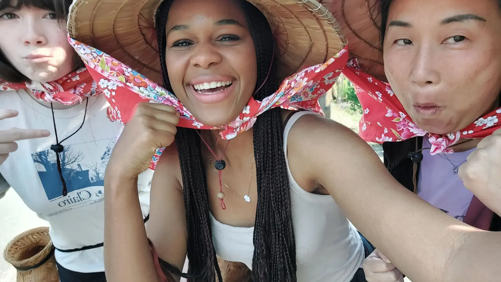 high school students playfully wrapping a red bandana around a classmate's face outdoors.
