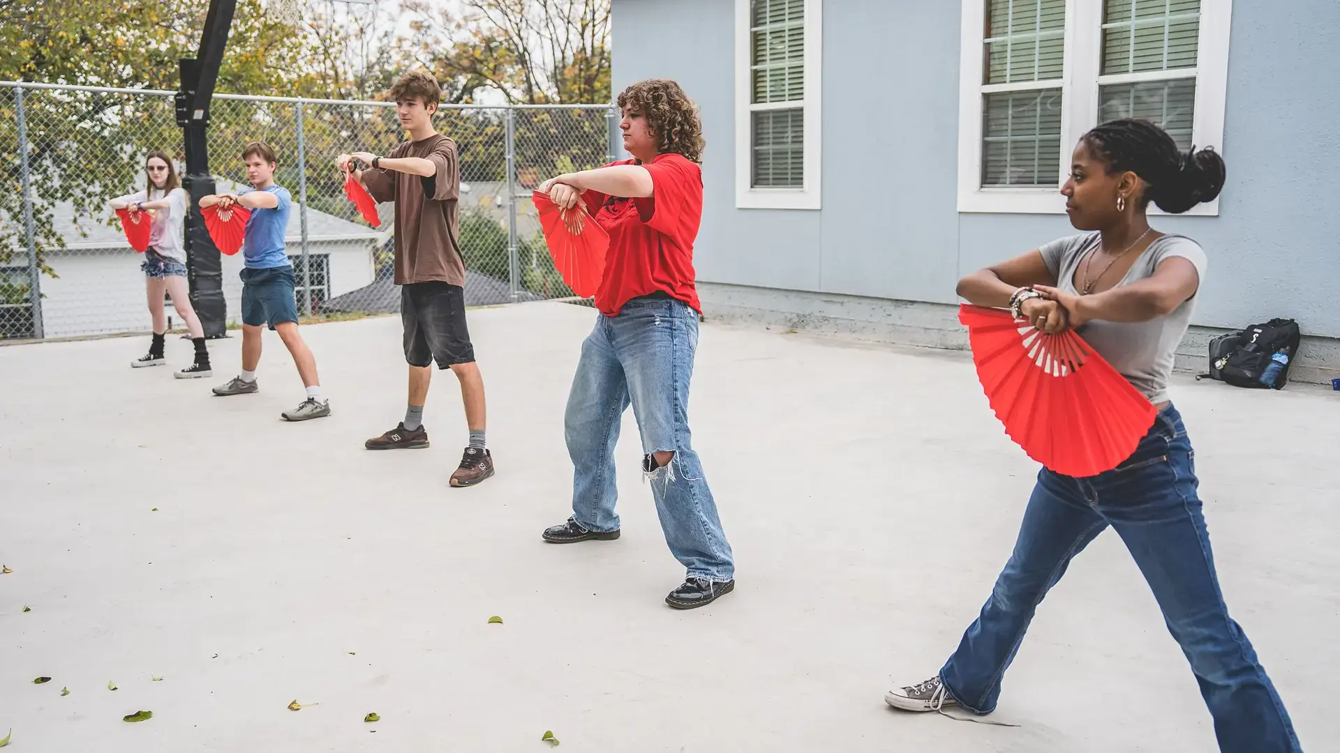 Students outdoors, one dancing with a red fan during a language class activity.