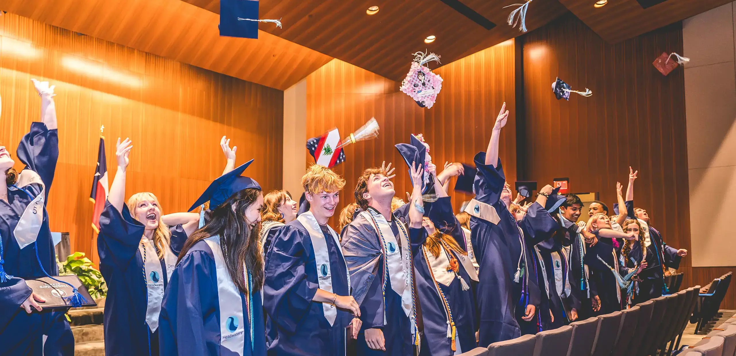 Headwaters School Class of 2025 graduates cheering and tossing their caps in the air during commencement.