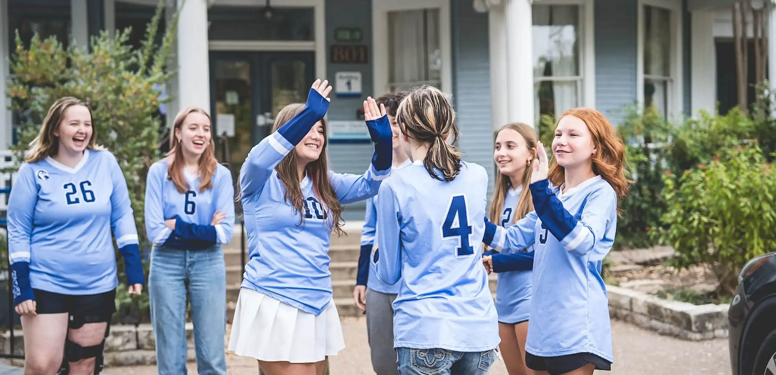 Student teammates celebrating together with high-fives while wearing school sports jerseys.
