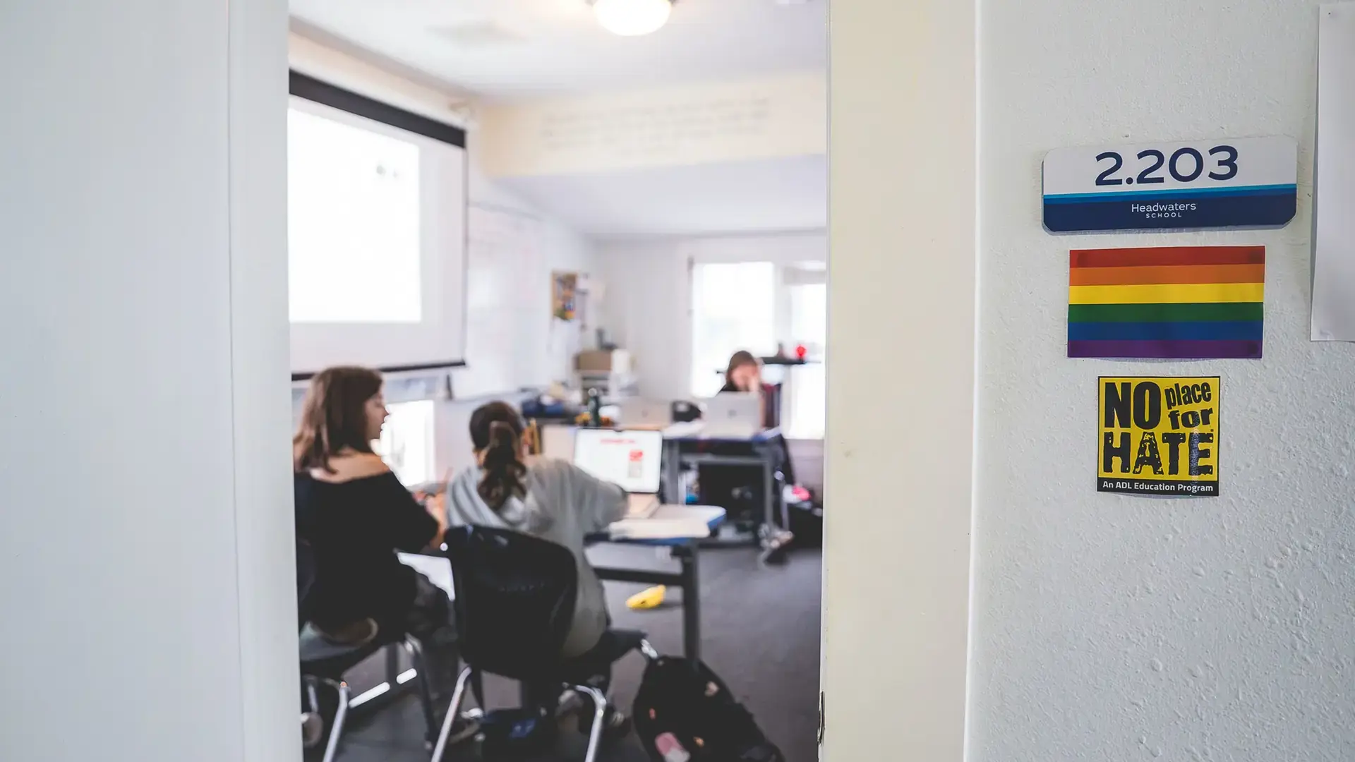 Students working at desks in a classroom with a 'No Place for Hate' sign on the wall.