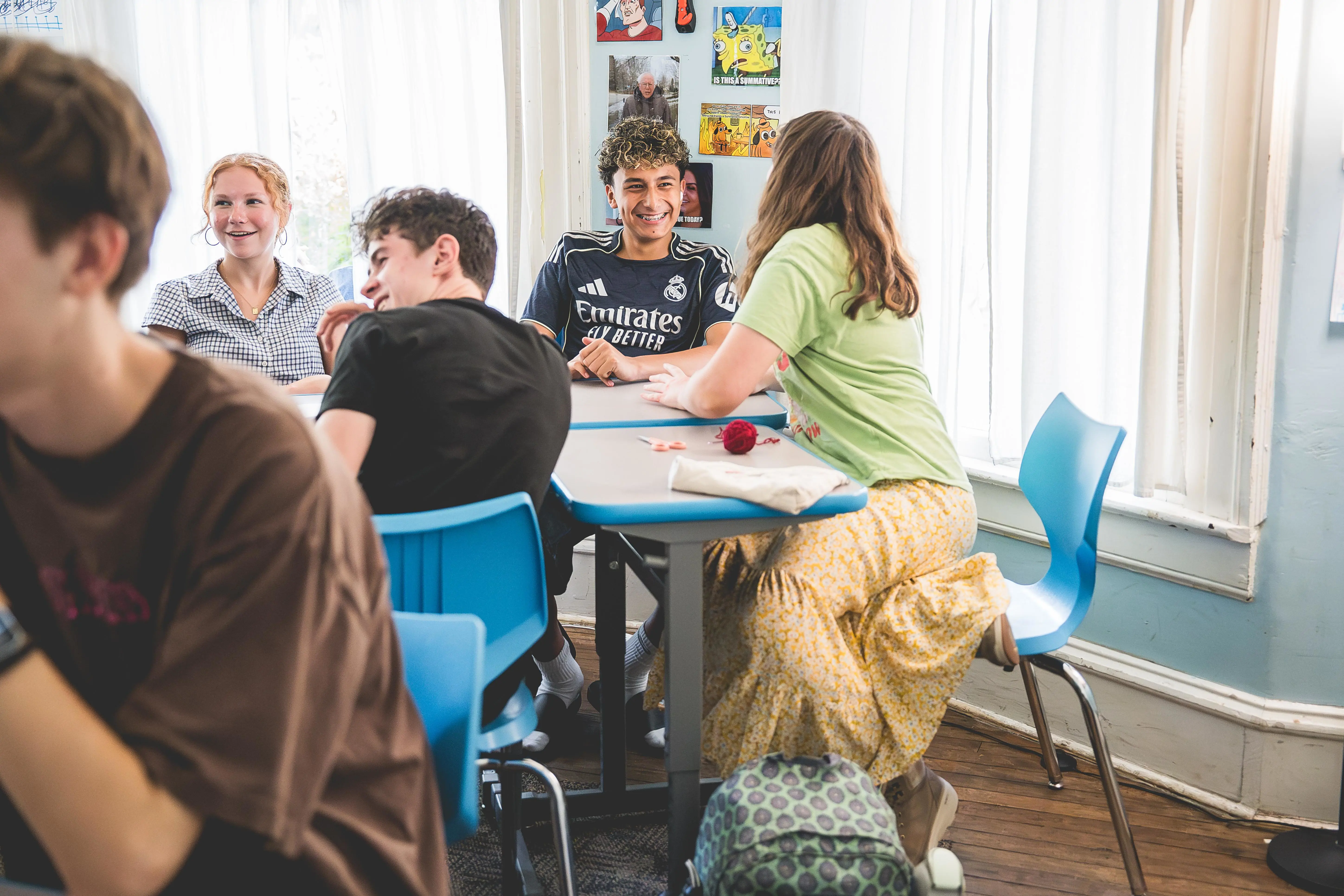 Students gathered around a classroom table, smiling and collaborating during a group discussion.