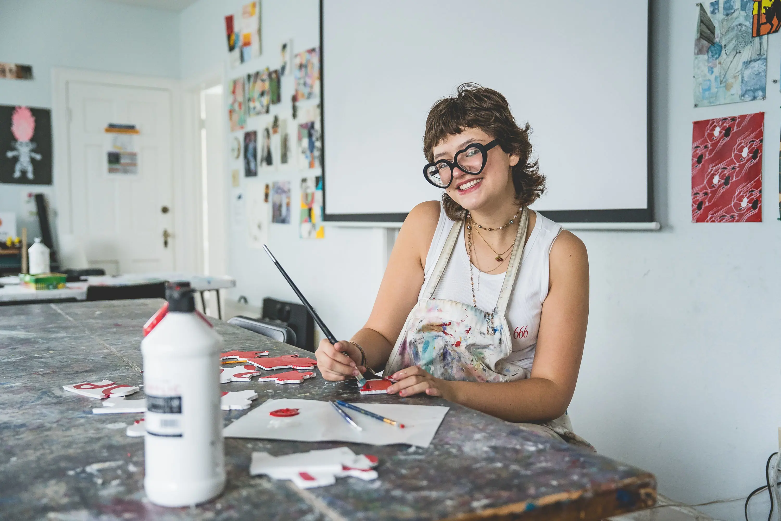 high school student smiling while working on a painting in the art studio.