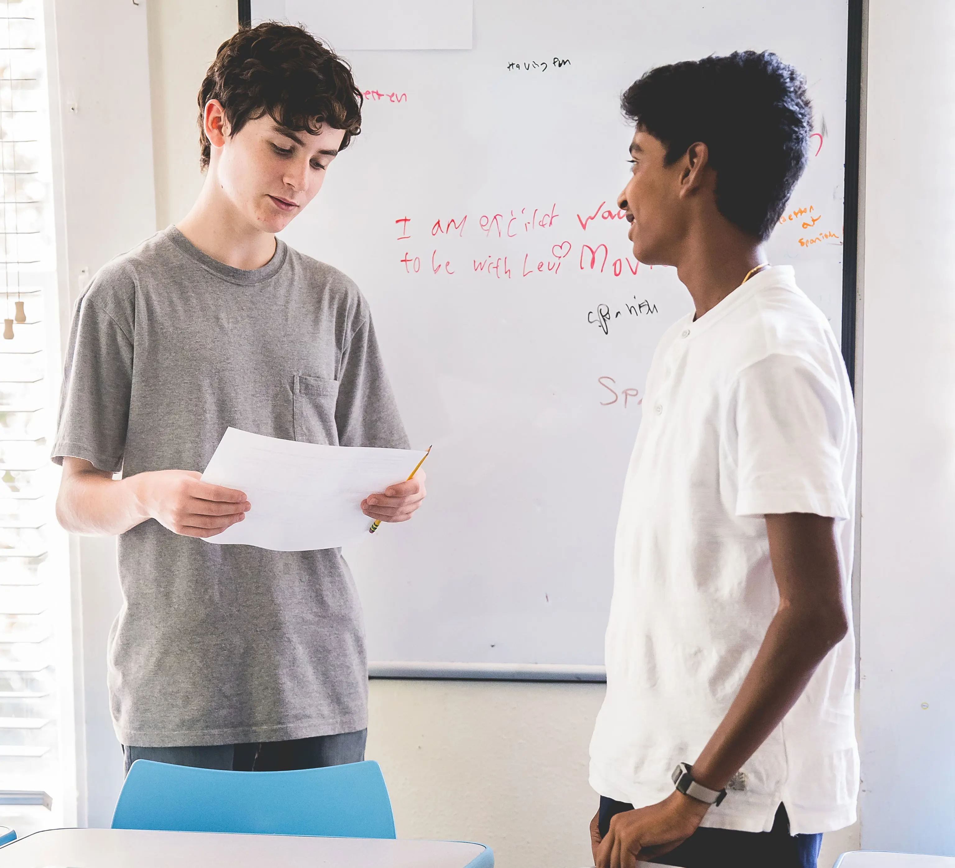 Two Headwaters high school students stand together in a classroom, reviewing notes and discussing an assignment during class at the River Campus.