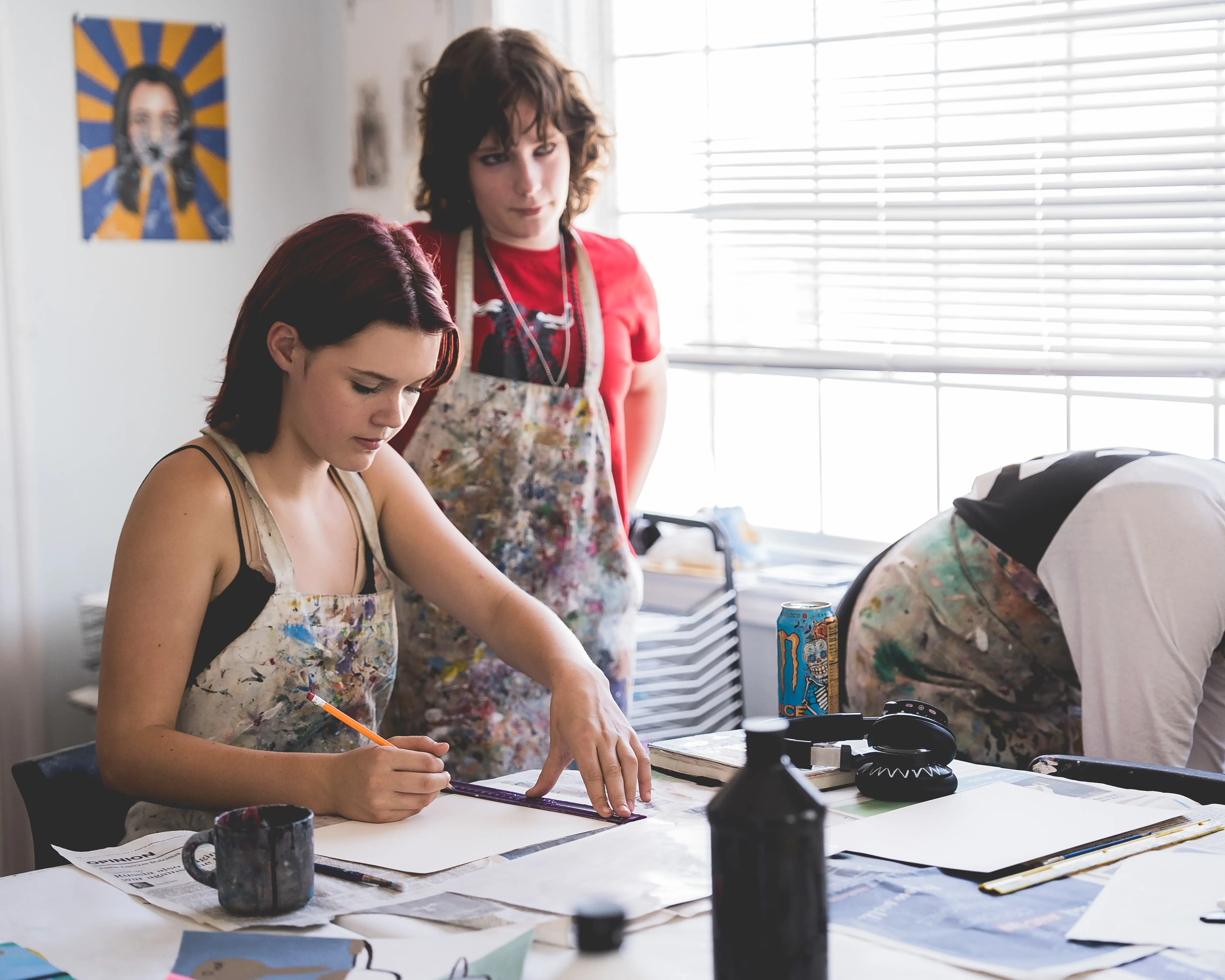 Headwaters High School students work on drawing projects in the visual arts studio while wearing paint aprons at the River Campus.