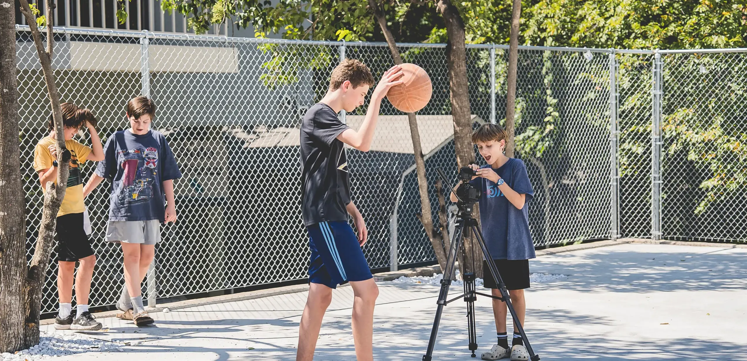 middle school students filming a classmate holding a basketball outdoors for a film class project.