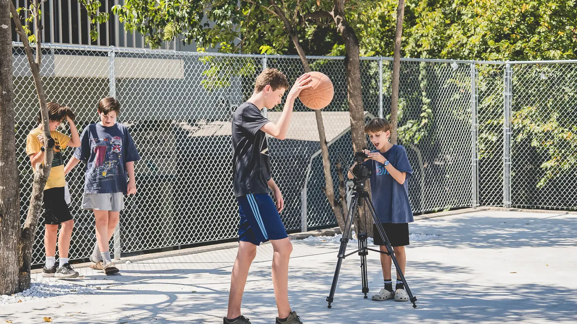 middle school students recording a basketball game on a tripod-mounted camera for a film class.