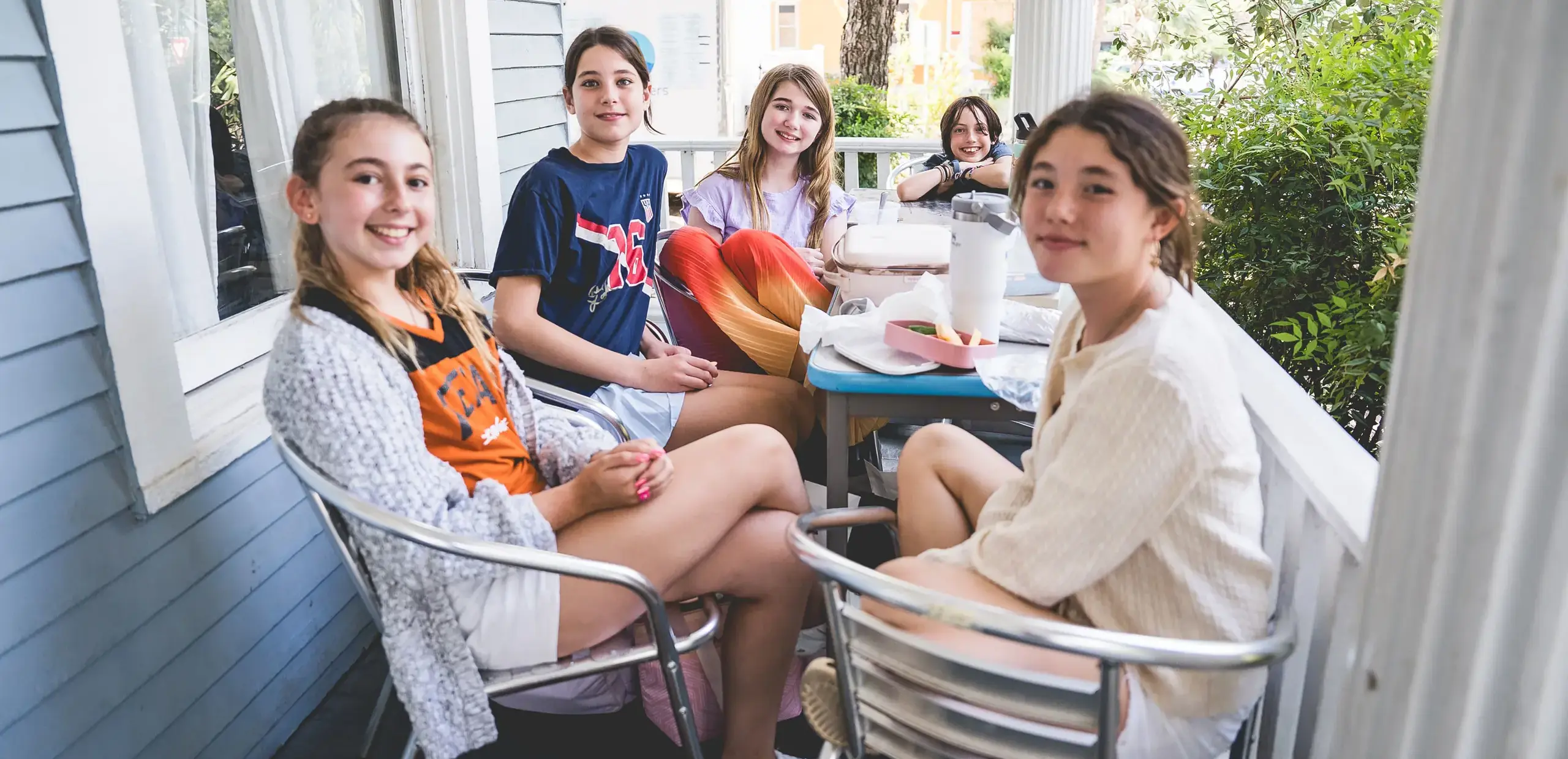 middle school students smiling together while eating lunch on an outdoor patio.