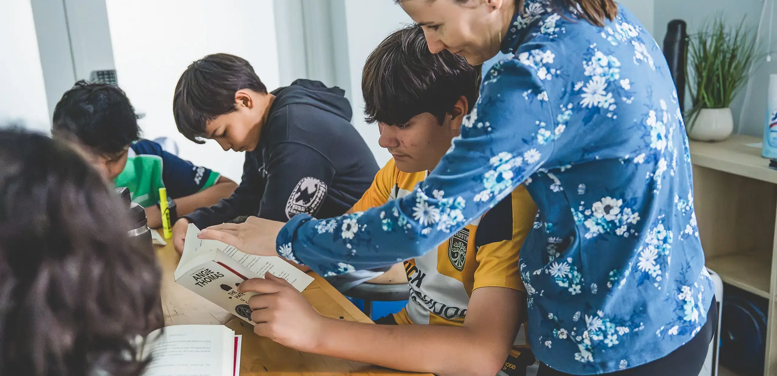 A teacher pointing to a book while guiding middle school students during a reading lesson.